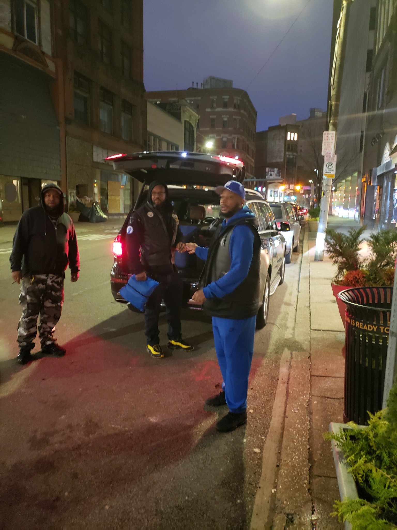 Three volunteers unloading blue supply bags from SUV on Pittsburgh street